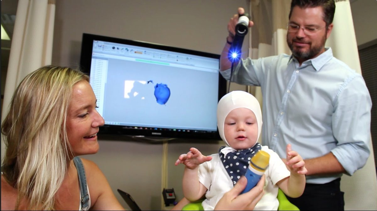A mother using a toy to keep her baby's attention while they are being scanned with a 3D scanner.