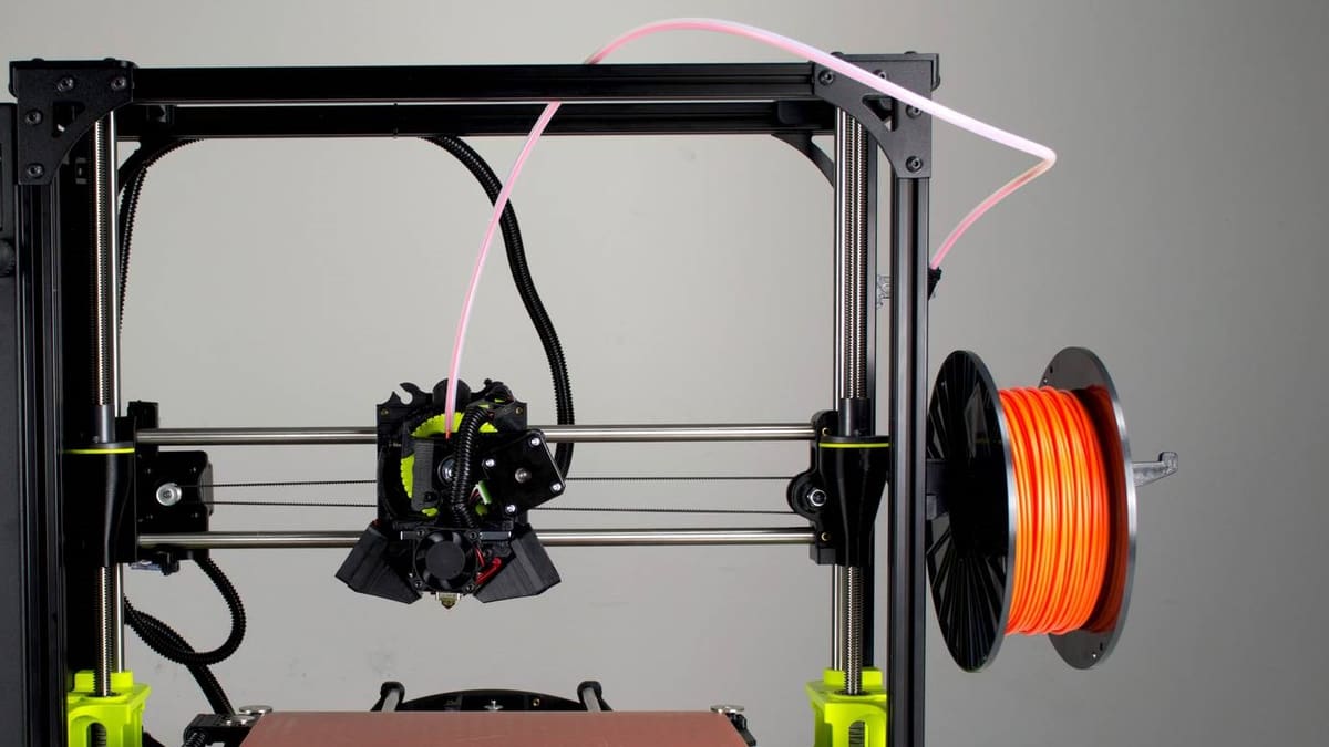 Orange filament being fed through the PTFE tube in a Bowden extrusion setup